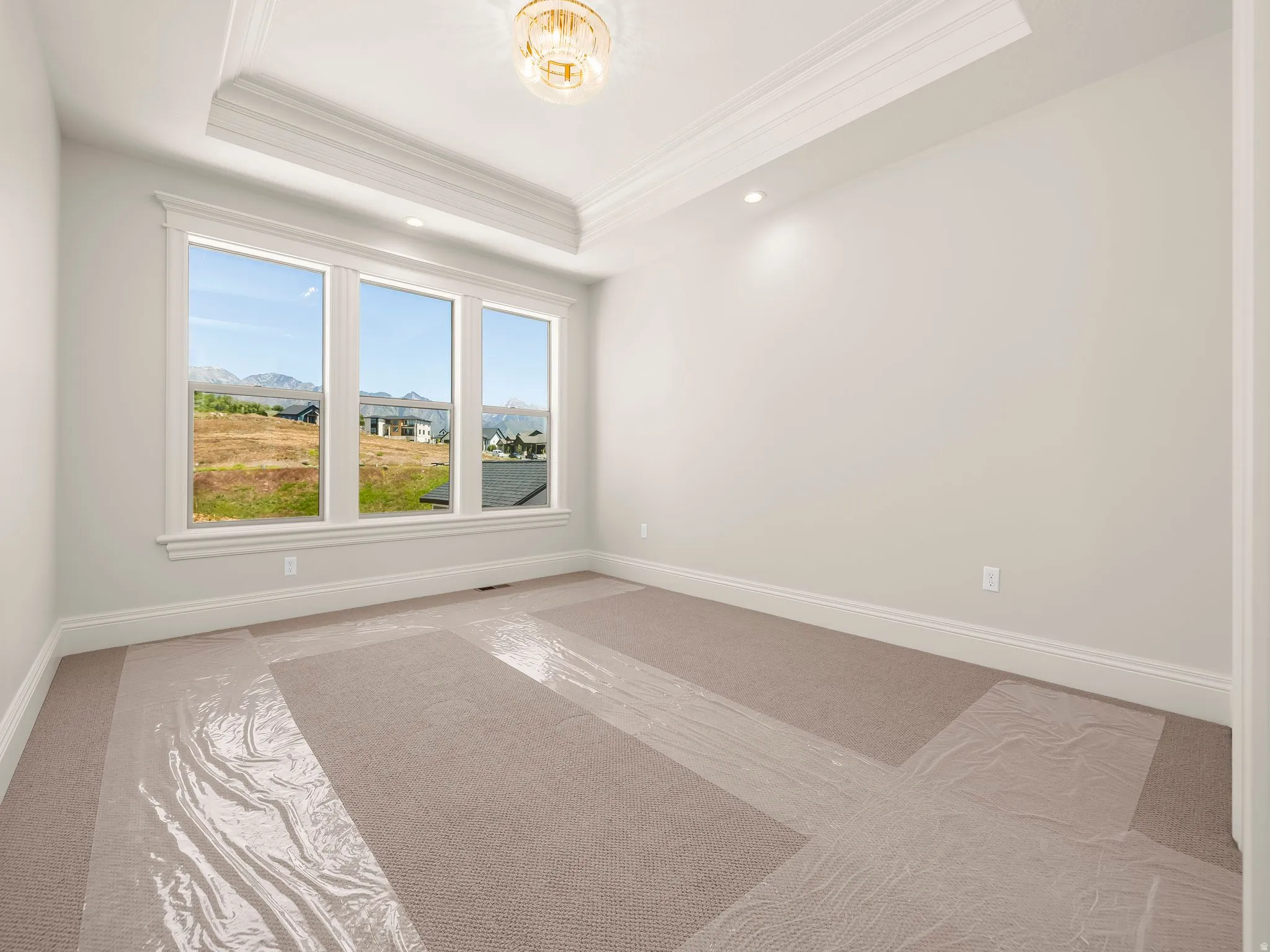 Light-filled room featuring a three-panel window, tray ceiling with crown molding, recessed lighting, and a decorative chandelier