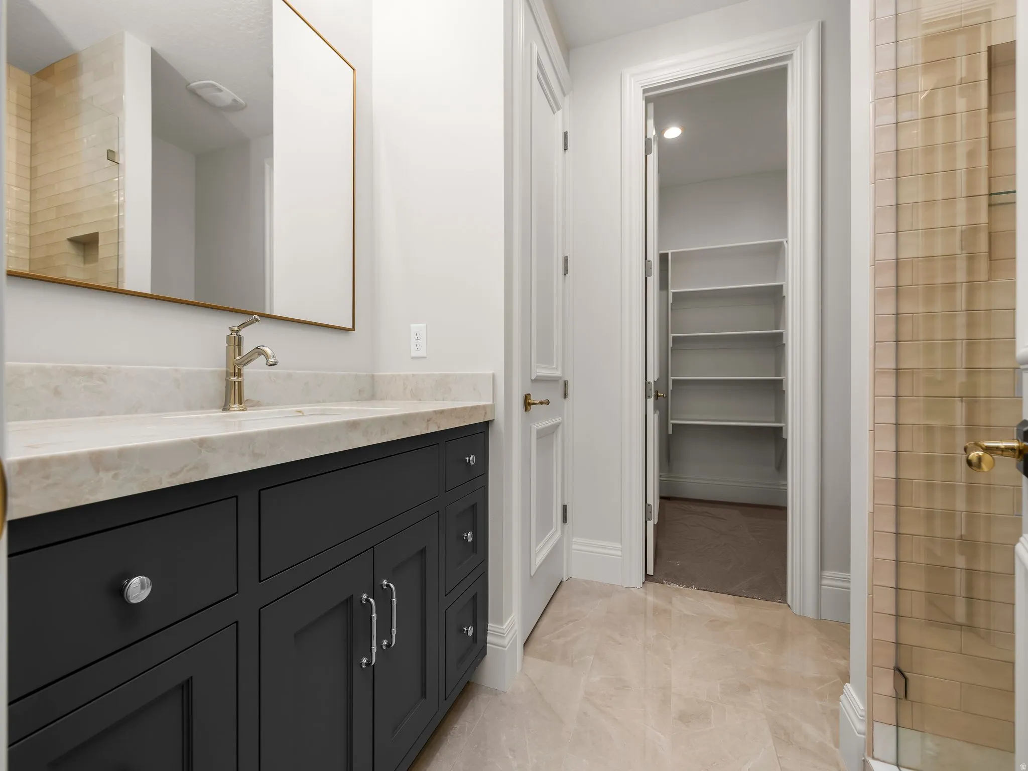 Bathroom vanity featuring a light-toned stone countertop, undermount sink, and brushed brass faucet