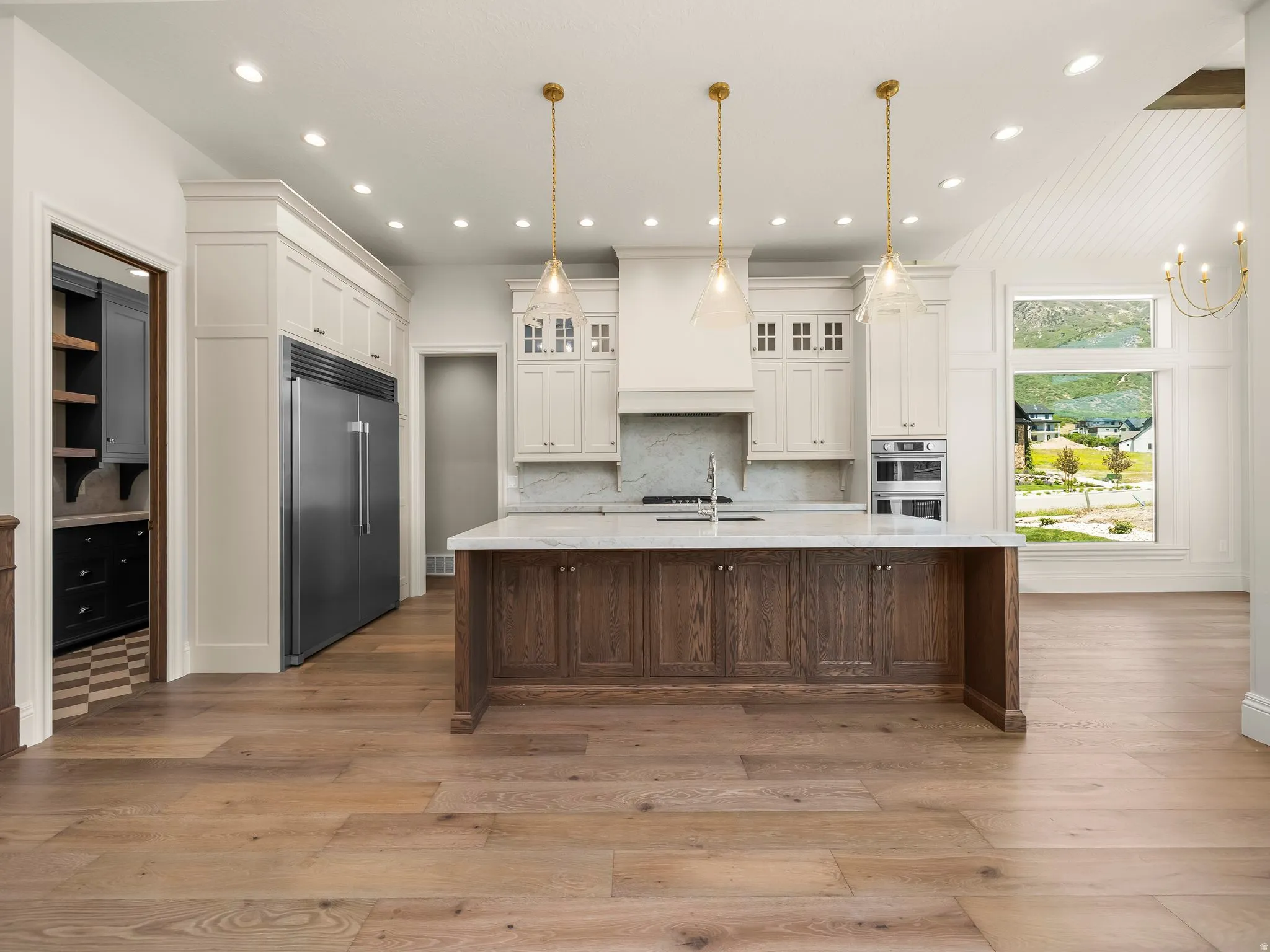 Expansive kitchen featuring a large wood-finish island with a stone countertop, brass pendant lighting, built-in stainless steel appliances, and wood-finish flooring
