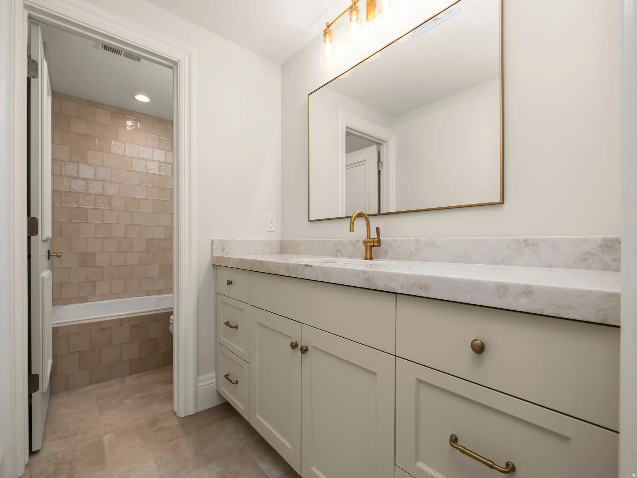 Bathroom vanity featuring a light-toned countertop with an undermount sink and a brass-finish faucet