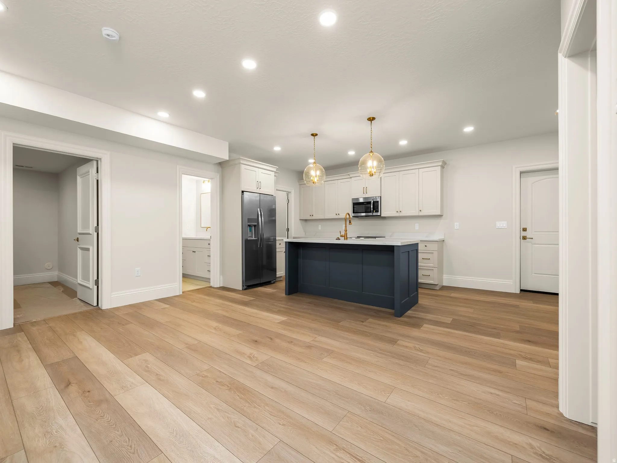 Open-concept kitchen with wood-finish flooring, recessed lighting, a dark blue island, white upper and lower cabinetry, and stainless steel appliances