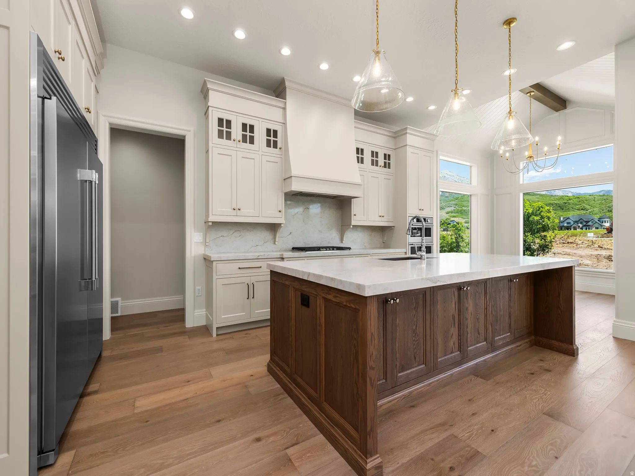 Kitchen featuring a large central island with a light-toned countertop, wood-finish flooring, white upper and lower cabinetry, stainless steel appliances, and ceiling-mounted lighting fixtures