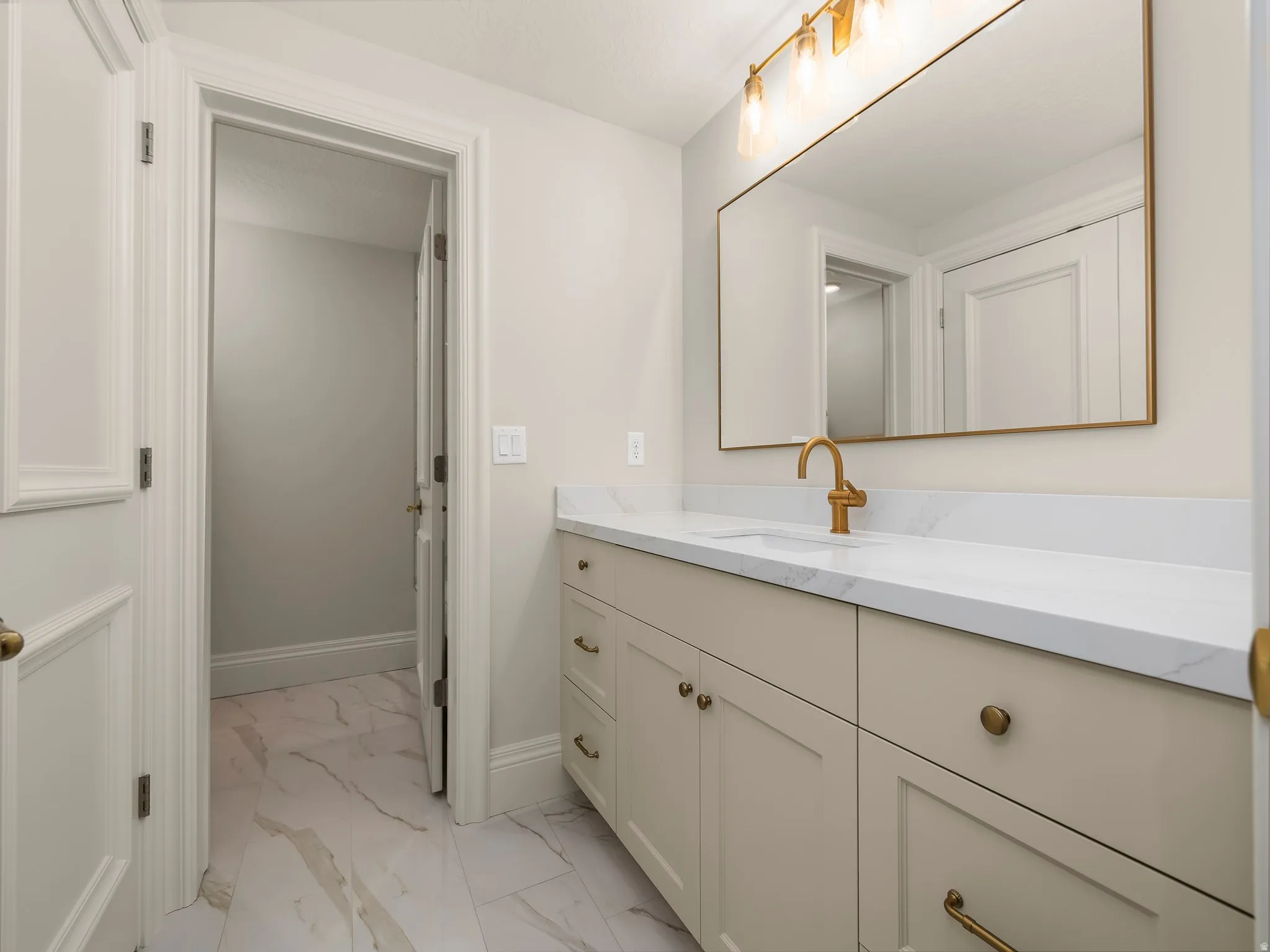 Bathroom vanity featuring a light-colored countertop, gold-toned faucet, and rectangular mirror with a gold frame