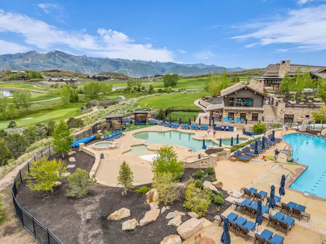 Expansive outdoor aquatic area featuring multiple pools, a hot tub, and an adjacent clubhouse with stone and wood siding