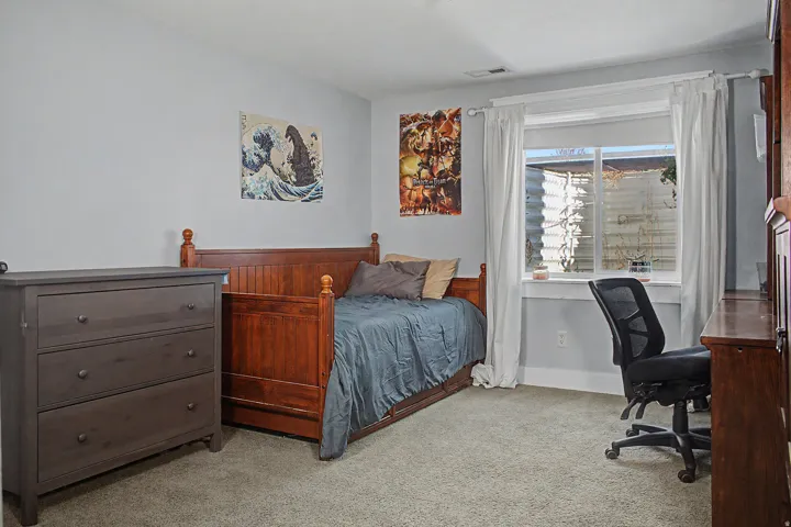 Carpeted room featuring a window with white drapes, light gray walls, and a built-in wooden desk