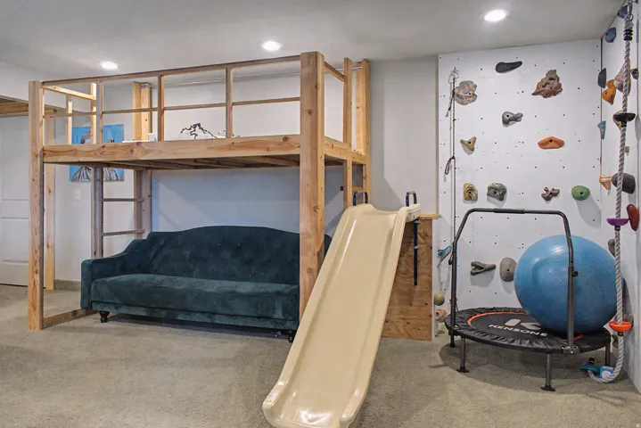 Recreational space featuring a built-in climbing wall with varied holds, a lofted wooden structure with a ladder, and recessed ceiling lighting