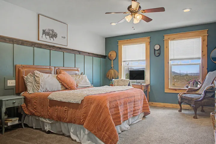 Bedroom featuring an upholstered accent wall with a wood beam, two windows with wood trim, and a ceiling fan with integrated lighting