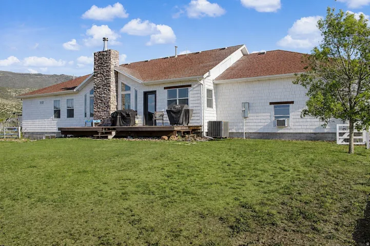 Rear exterior featuring a spacious wood deck, white shingle siding, and a prominent stone-clad chimney
