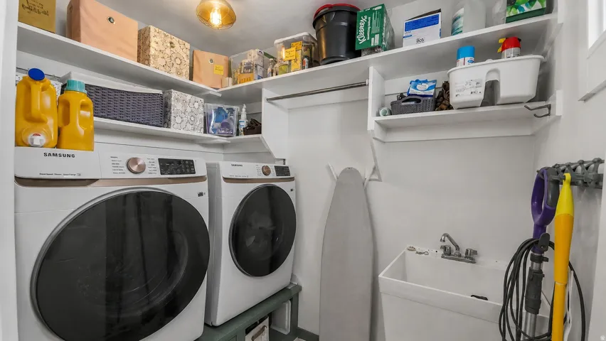 Dedicated laundry area featuring a front-loading washer and dryer set, corner shelving, utility sink with faucet, and a wall-mounted hanging rod