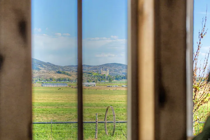 Expansive rural landscape featuring green fields, distant mountains, and agricultural structures