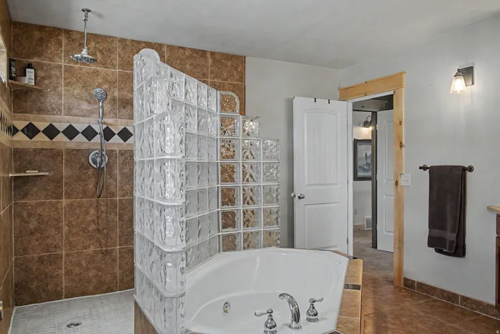 Bathroom featuring a corner jetted soaking tub, glass block partition, and a tiled shower enclosure with a rainfall showerhead