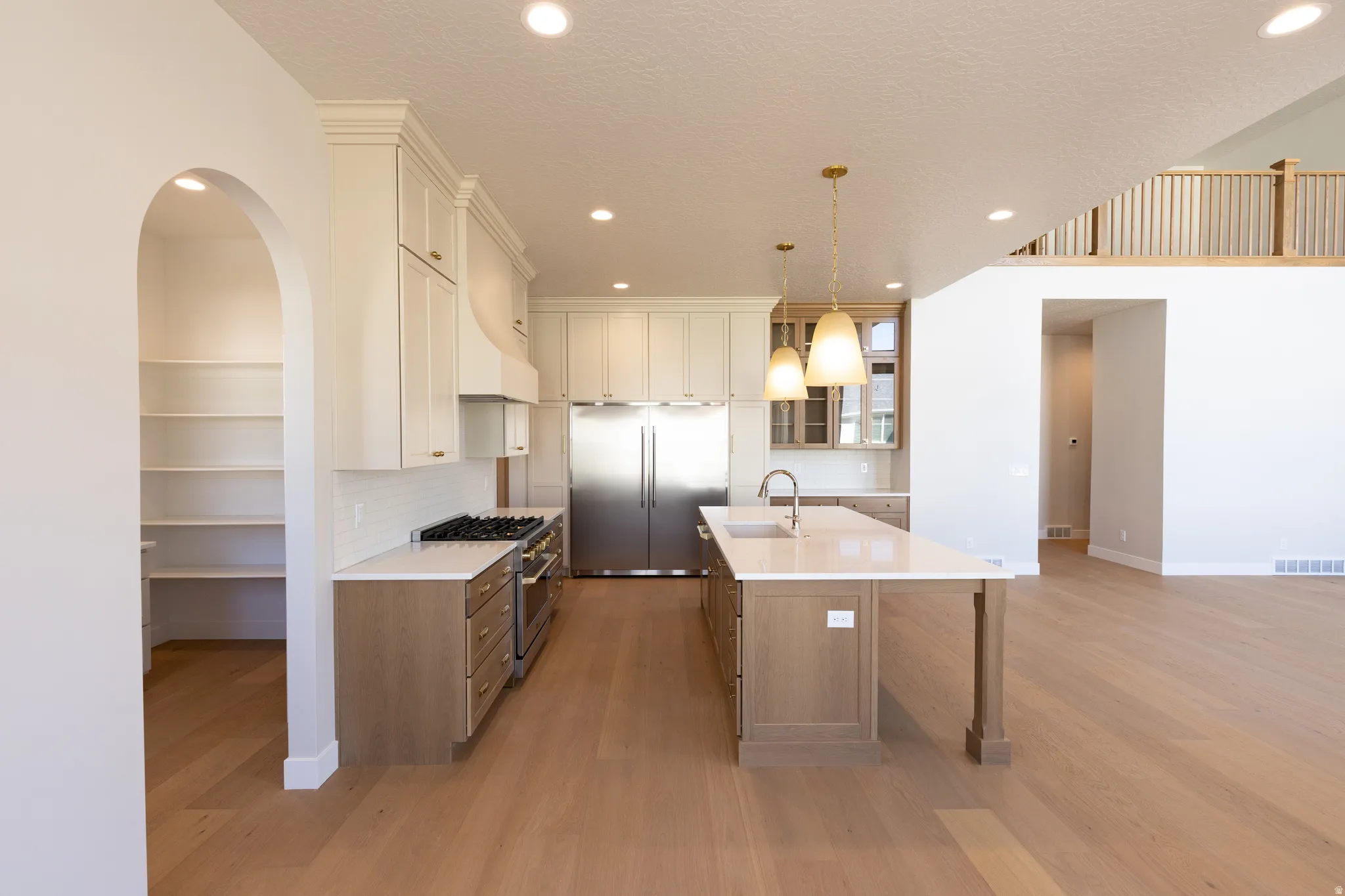 Contemporary kitchen featuring a large central island with sink, stainless steel appliances, white subway tile backsplash, and a walk-in pantry with built-in shelving