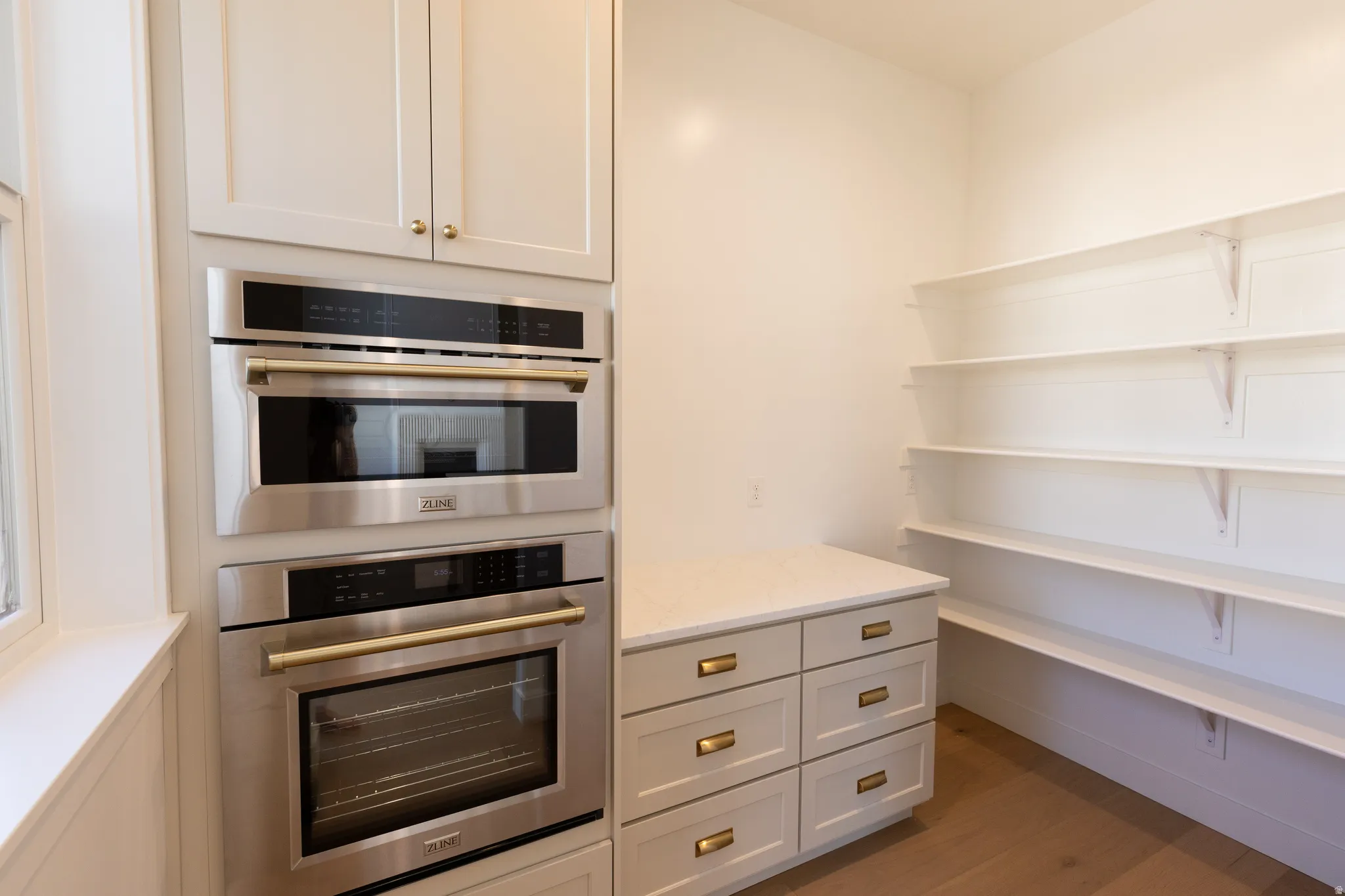 Dedicated pantry space featuring extensive shelving, built-in cabinetry with brass hardware, and a stone countertop
