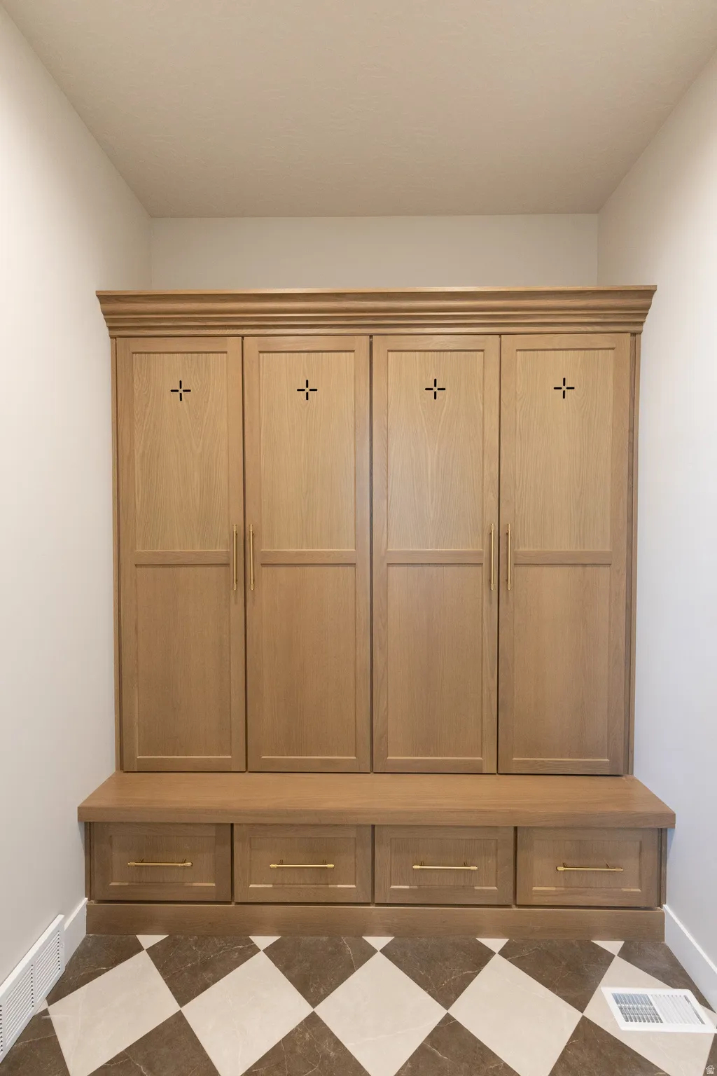 Built-in wood-finish cabinetry featuring four upper storage units with cross-detail accents, four lower drawers, and a built-in bench