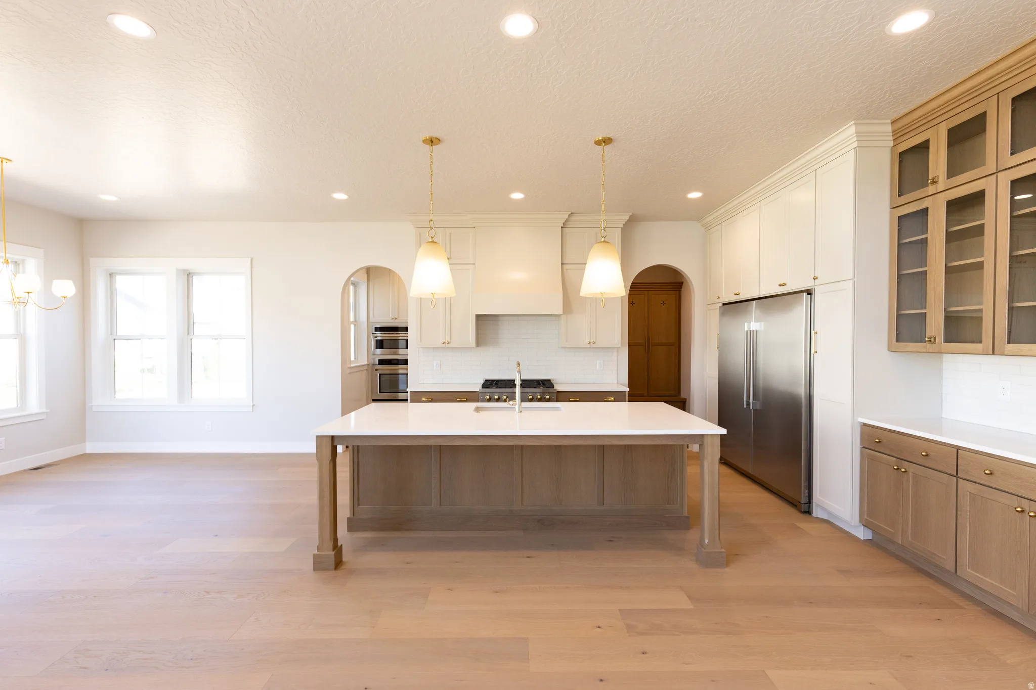 Open-concept kitchen featuring a large central island with a light-toned countertop, stainless steel appliances, a white subway tile backsplash, and light wood-finish flooring