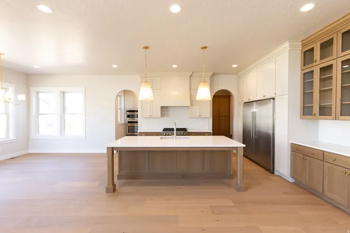Open-concept kitchen featuring a large central island with a light-toned countertop, stainless steel appliances, a white subway tile backsplash, and light wood-finish flooring