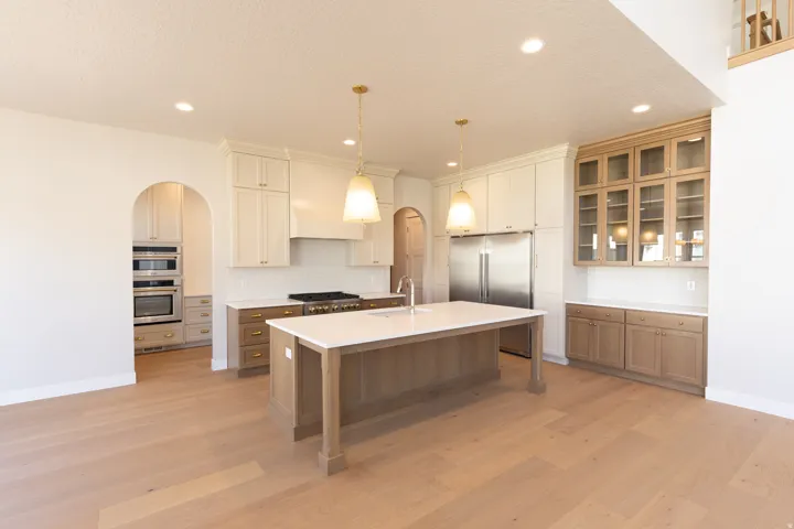 Gourmet kitchen featuring a large central island with a sink, stainless steel appliances, a gas range with an overhead vent hood, ample cabinetry in varied finishes, and light wood-finish flooring