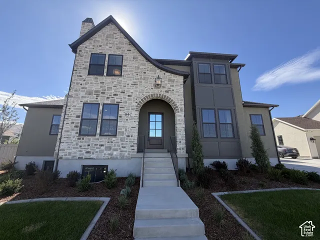 Stone and stucco exterior with an arched entryway, dark trim windows, and a concrete pathway leading to the front door