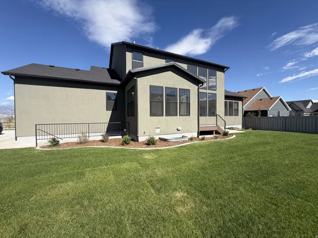 Expansive green lawn, stucco exterior, multiple large windows, ground-level planting beds, and a perimeter privacy fence