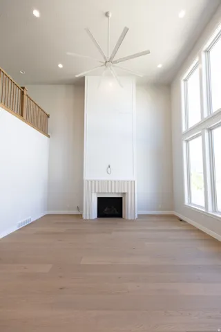 Spacious living area featuring a floor-to-ceiling fireplace with reeded paneling, high ceilings with recessed lighting, a multi-blade ceiling fan, expansive windows, and light wood-finish flooring
