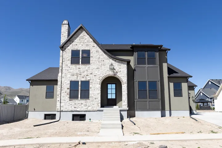 Stone and stucco exterior featuring an arched entryway, prominent chimney, bay window, dark window frames, and a shingle roof