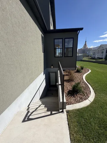 Exterior entrance with concrete stairs, dark-framed windows, and an adjacent lawn area