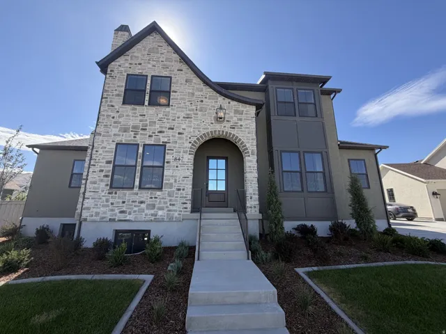 Stone and stucco exterior with an arched entryway, dark trim windows, and a concrete pathway leading to the front door