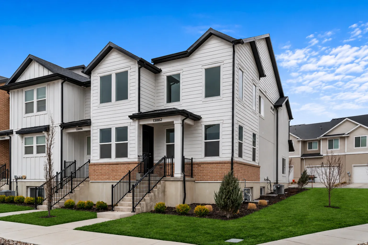Contemporary townhome exterior featuring white siding, black trim, a brick facade accent, and black metal railings leading to the front entry