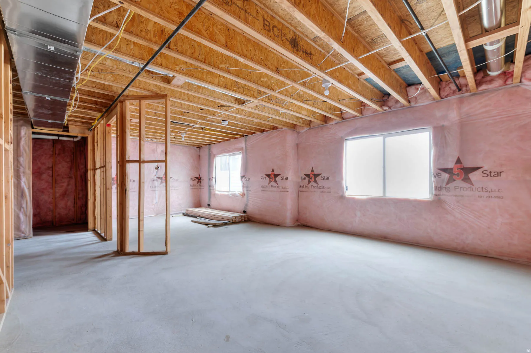 Unfinished basement featuring exposed wood joists, framed interior walls, concrete flooring, and two windows