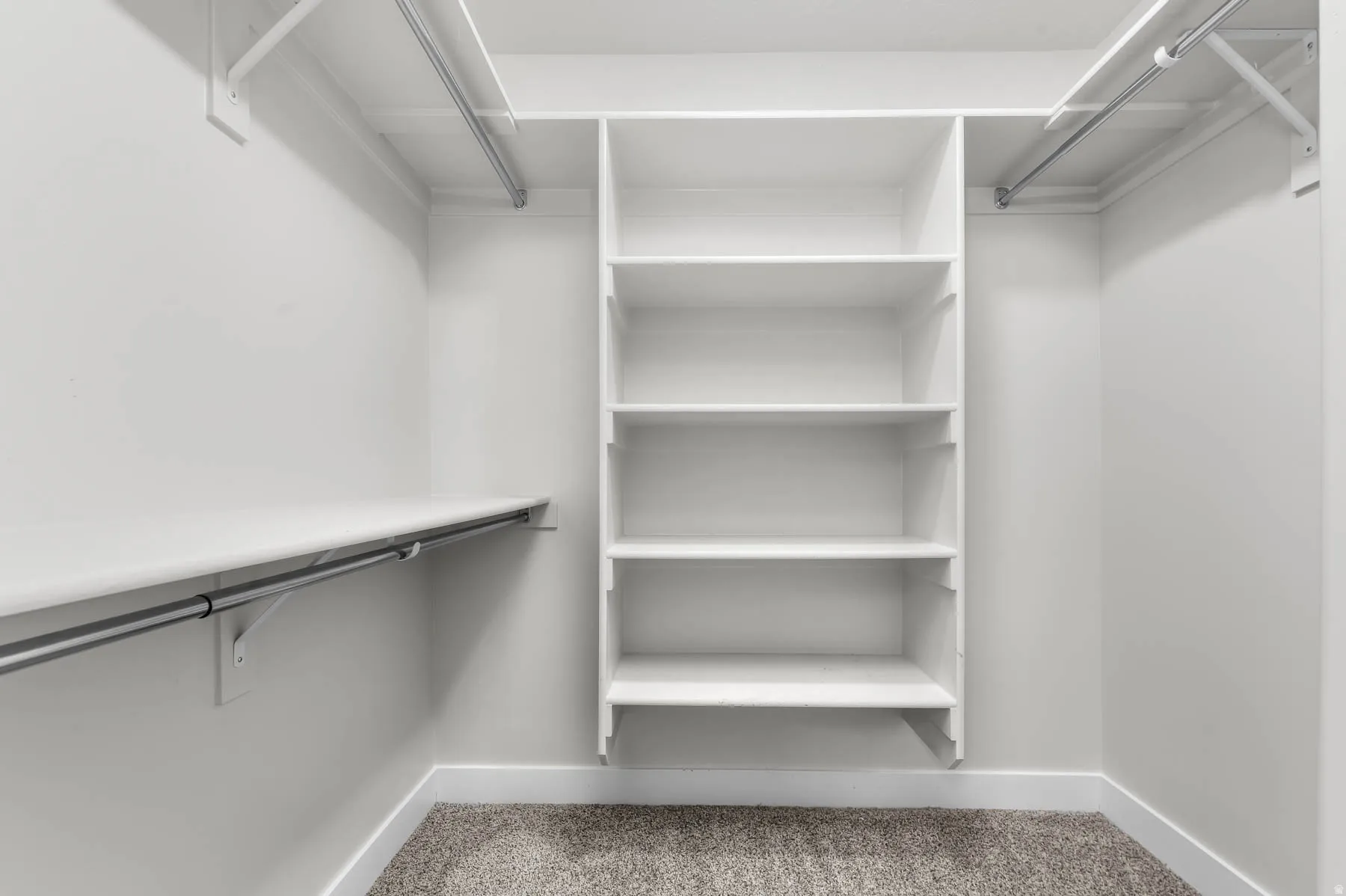 Walk-in closet featuring white built-in shelving, white walls, and light-colored carpeting
