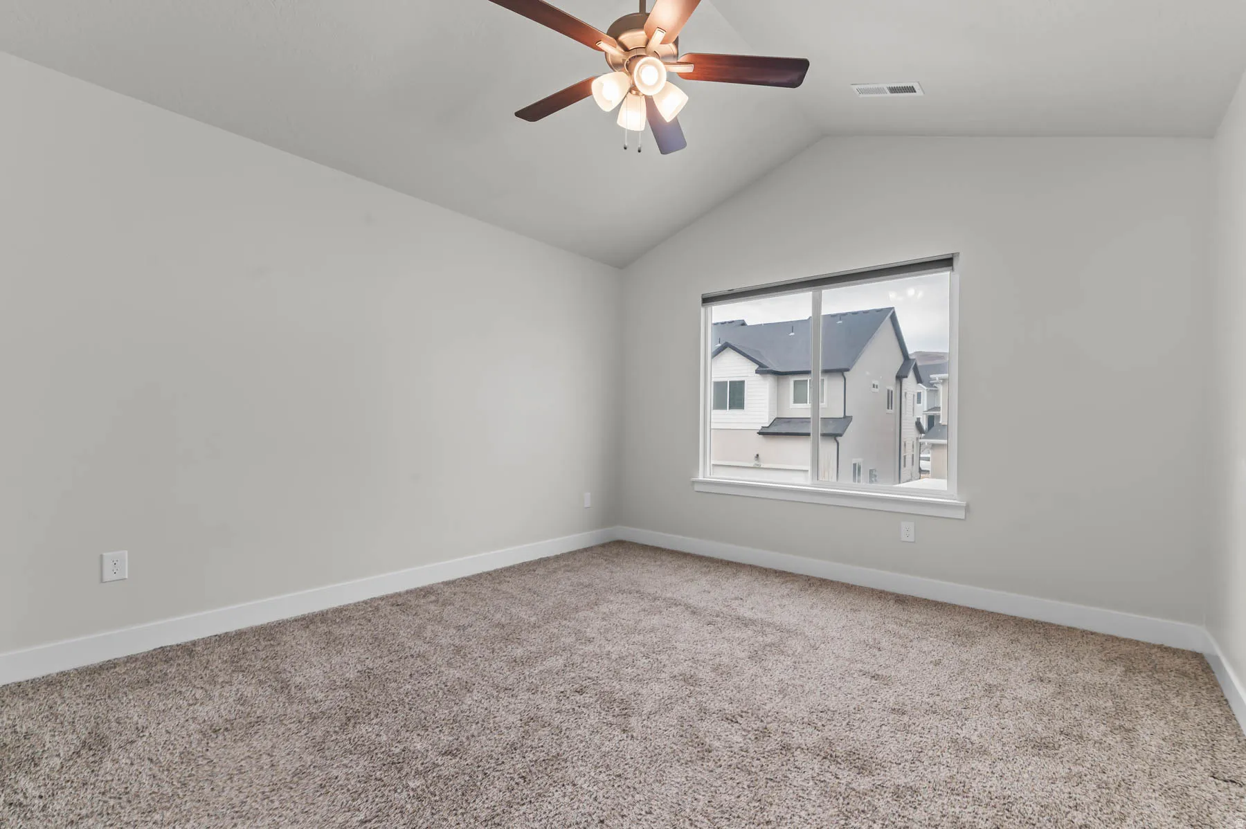 Carpeted room featuring a vaulted ceiling with a ceiling fan, a large window, and white trim
