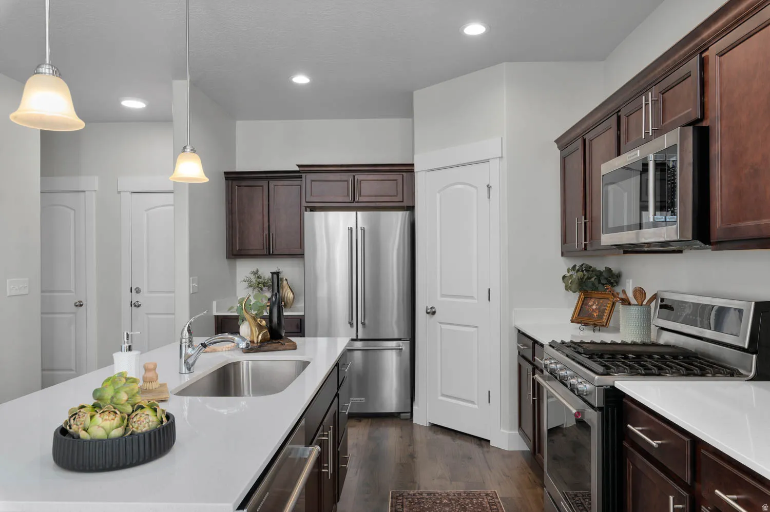 Kitchen featuring an expansive island with an undermount sink, pendant lighting, stainless steel appliances, dark wood cabinetry, and wood-finish flooring