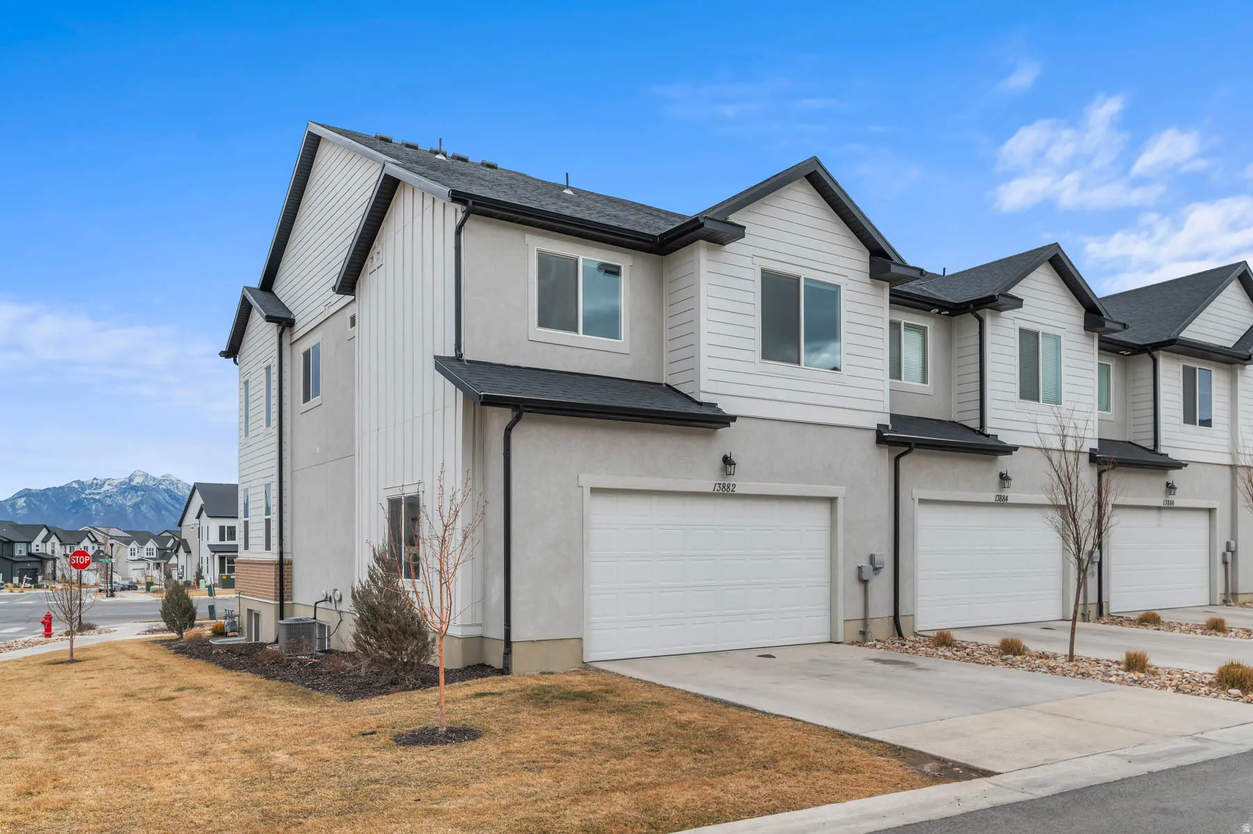 End-unit townhome featuring a two-car garage, white siding, light stucco, and dark shingle roofing