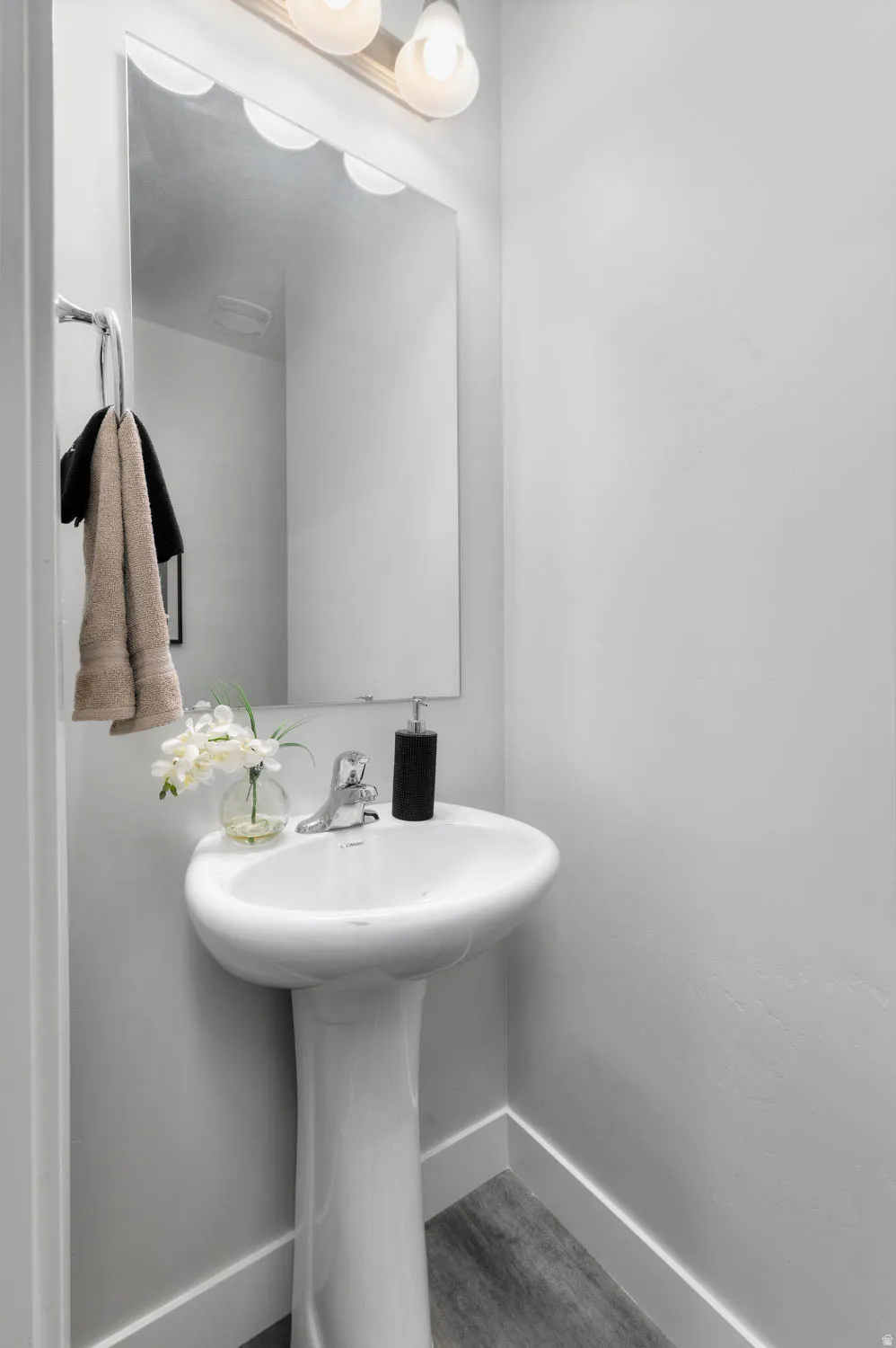 Pedestal sink with chrome faucet, large frameless mirror, and a three-light vanity fixture