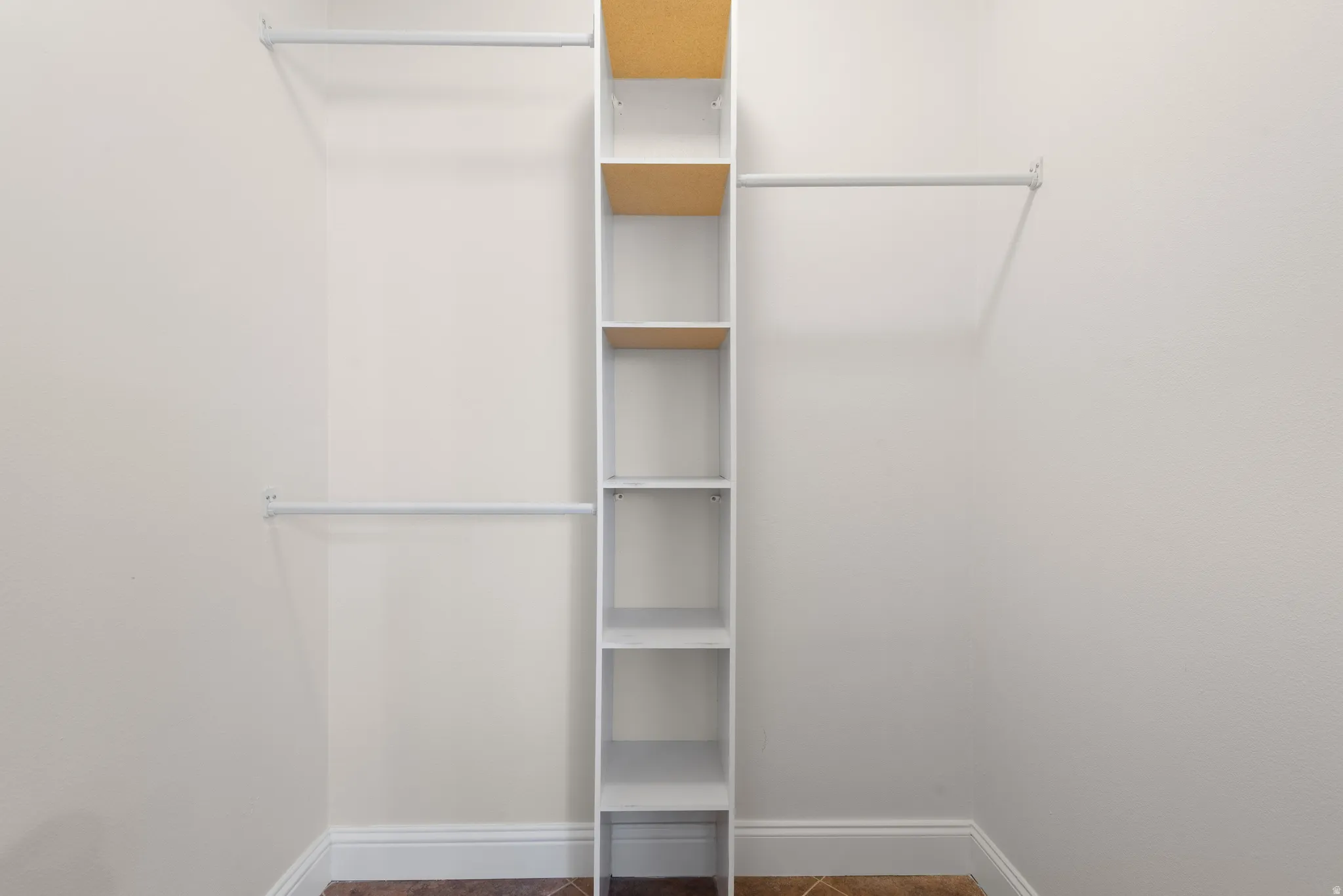 Closet featuring a built-in shelving unit, multiple clothing rods, light-toned wall paint, white baseboards, and tile flooring