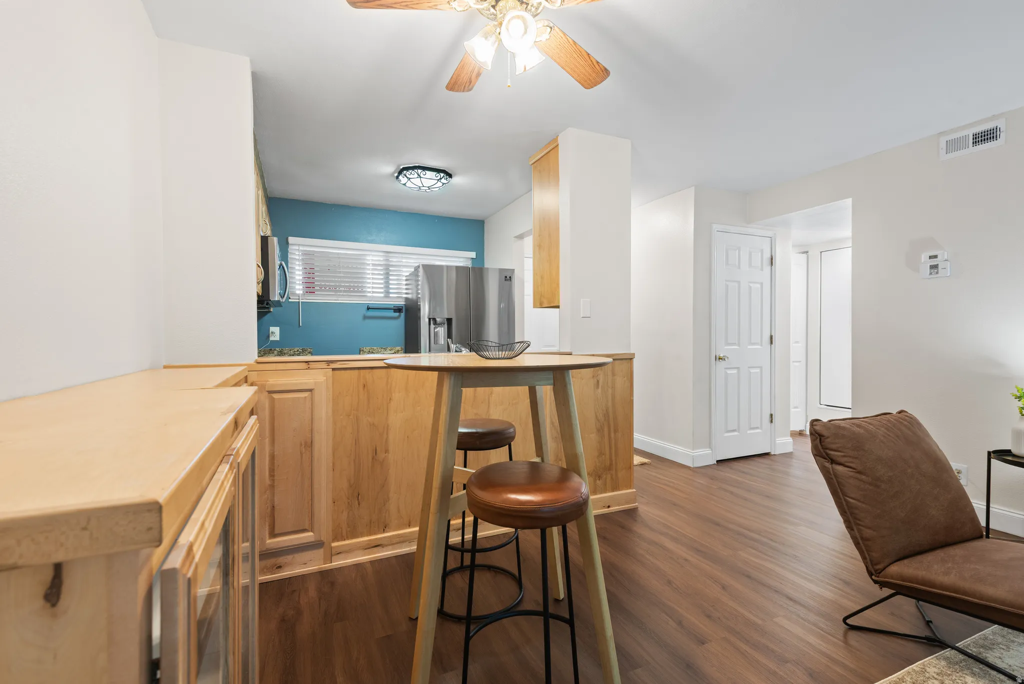 Open-concept kitchen and living area featuring wood-finish flooring, light wood cabinetry, white trim, and a ceiling fan with integrated lighting