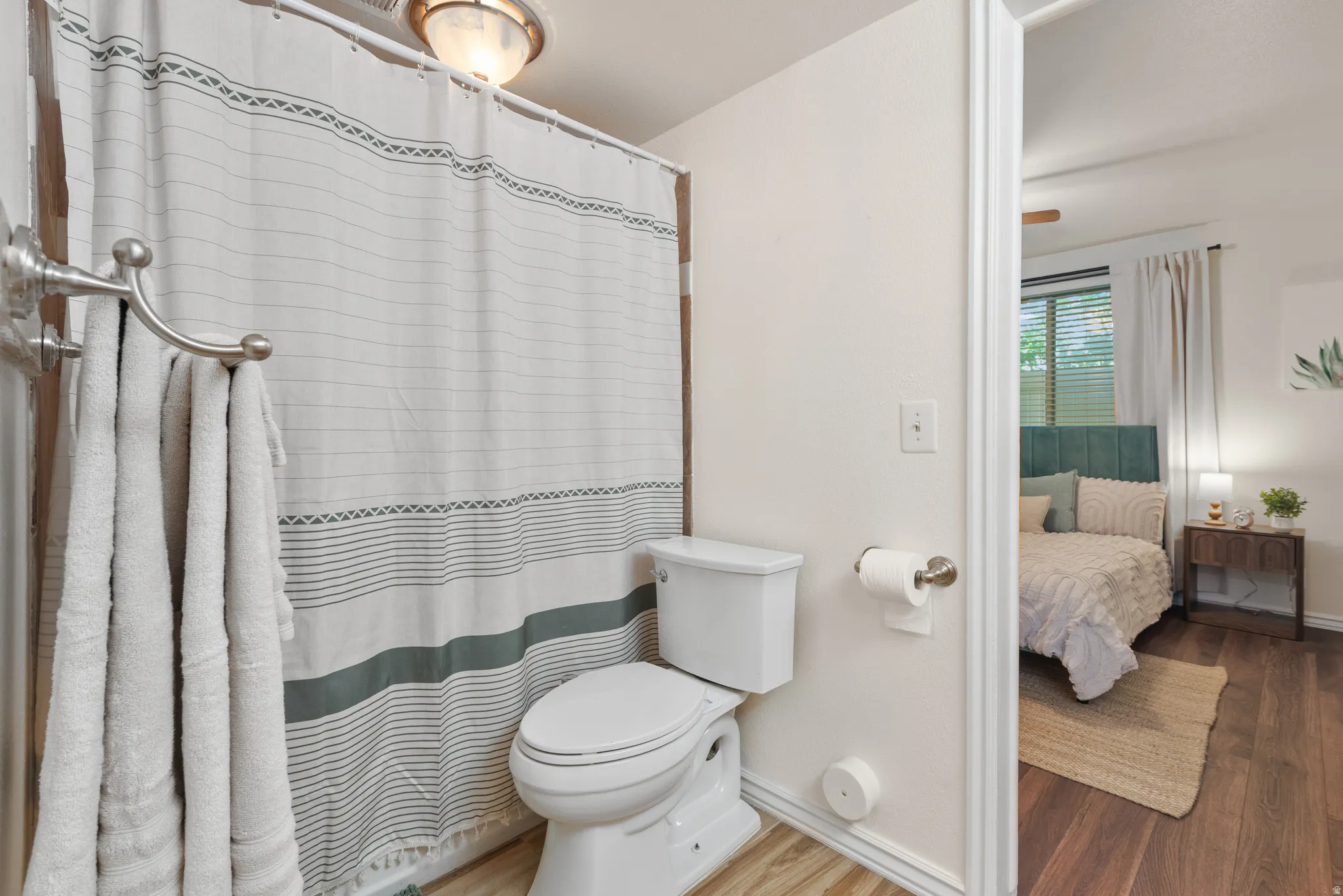 Bathroom featuring a white toilet, shower with a curved rod, and wood-finish flooring