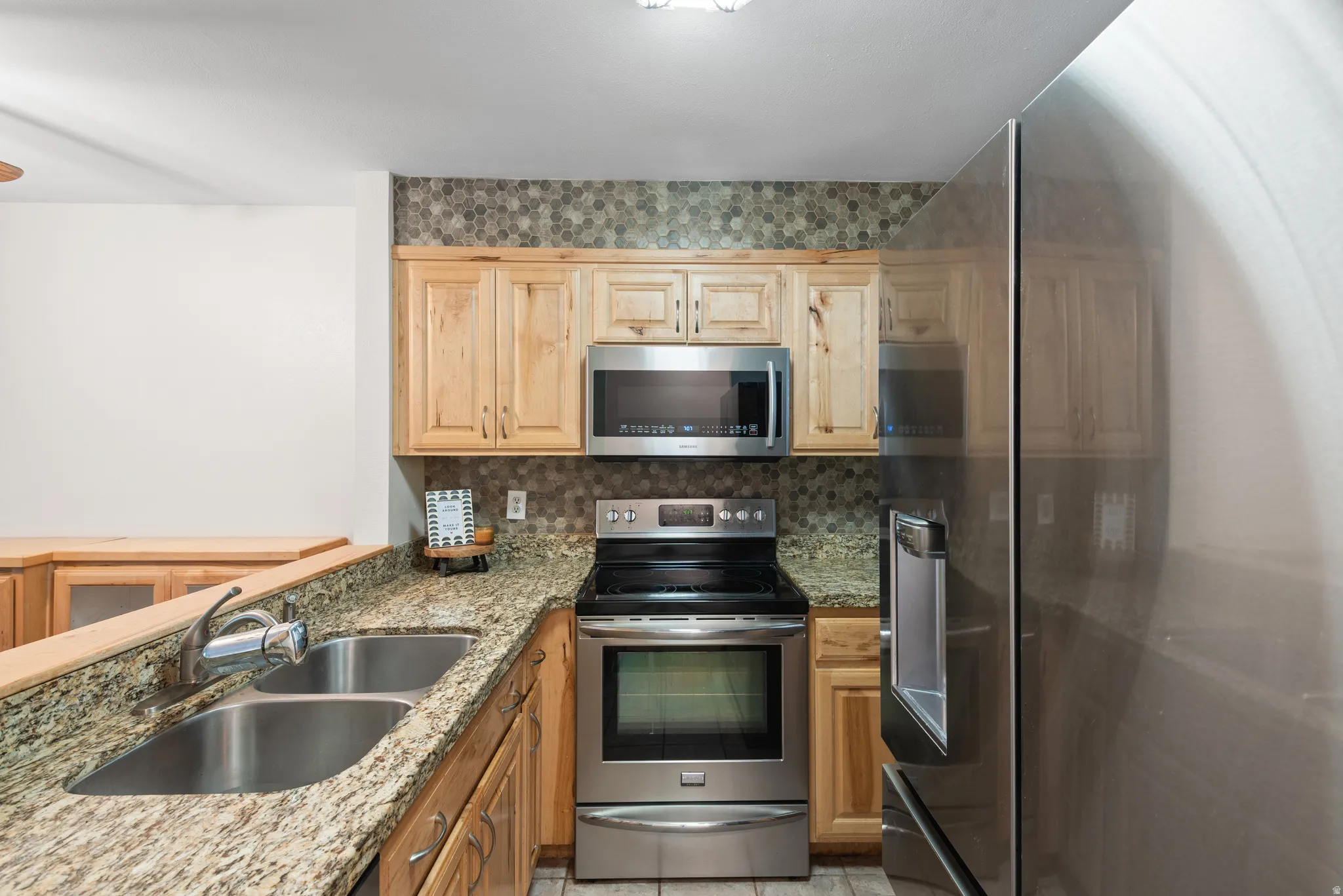 Kitchen featuring granite countertops, wood cabinetry, stainless steel appliances, a double basin sink, and a hexagonal tile backsplash