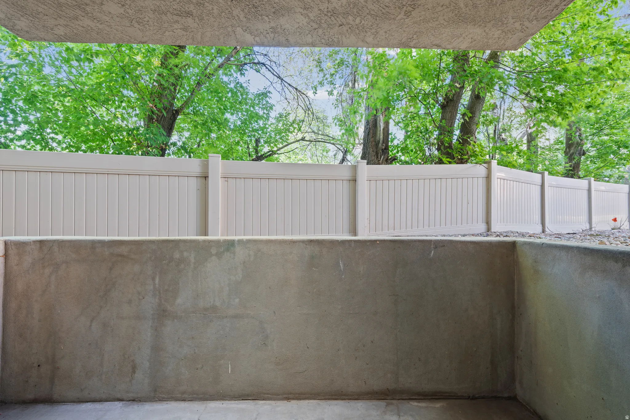Private concrete patio featuring a perimeter privacy fence, retaining wall, and mature trees beyond