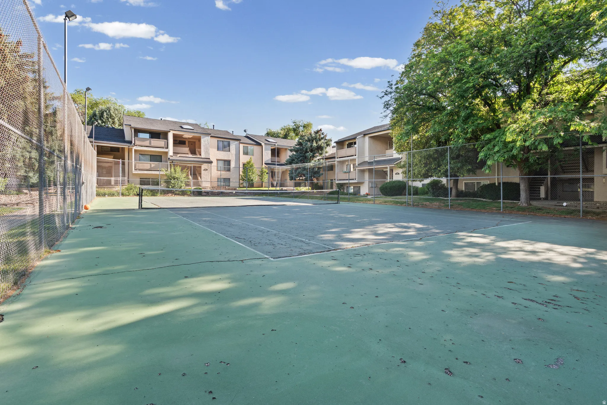 On-site tennis court with chain-link fencing, surrounded by mature trees and multi-story residential buildings