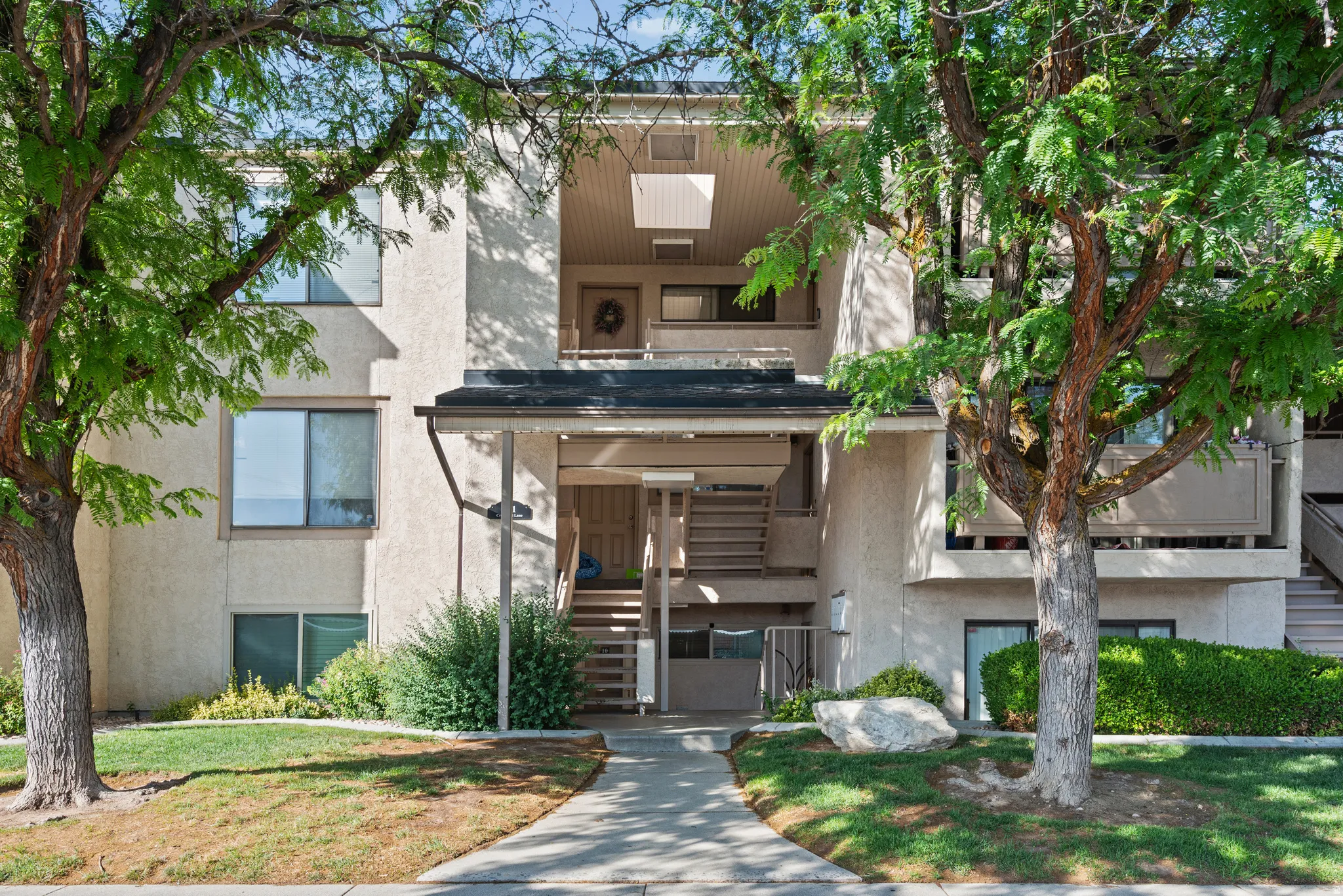 Multi-level residential building featuring stucco exterior, prominent entryways with stairs, and multiple private balconies
