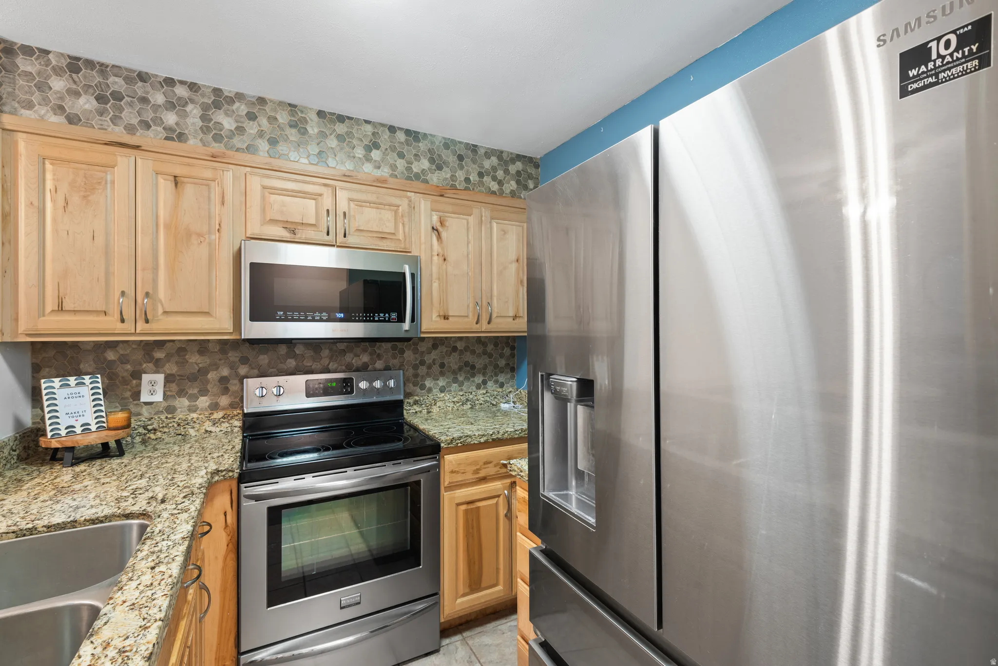 Kitchen featuring wood cabinetry, stainless steel appliances, granite countertops, and a hexagonal tile backsplash