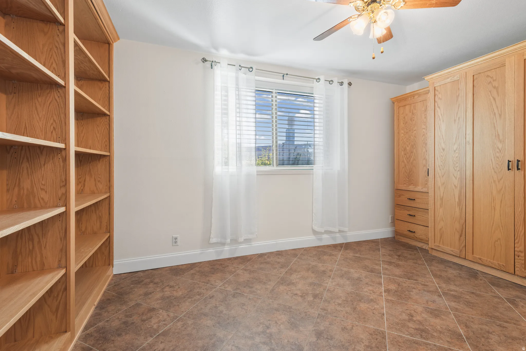 Room featuring extensive built-in shelving, a window with horizontal blinds, and a built-in cabinetry unit with drawers