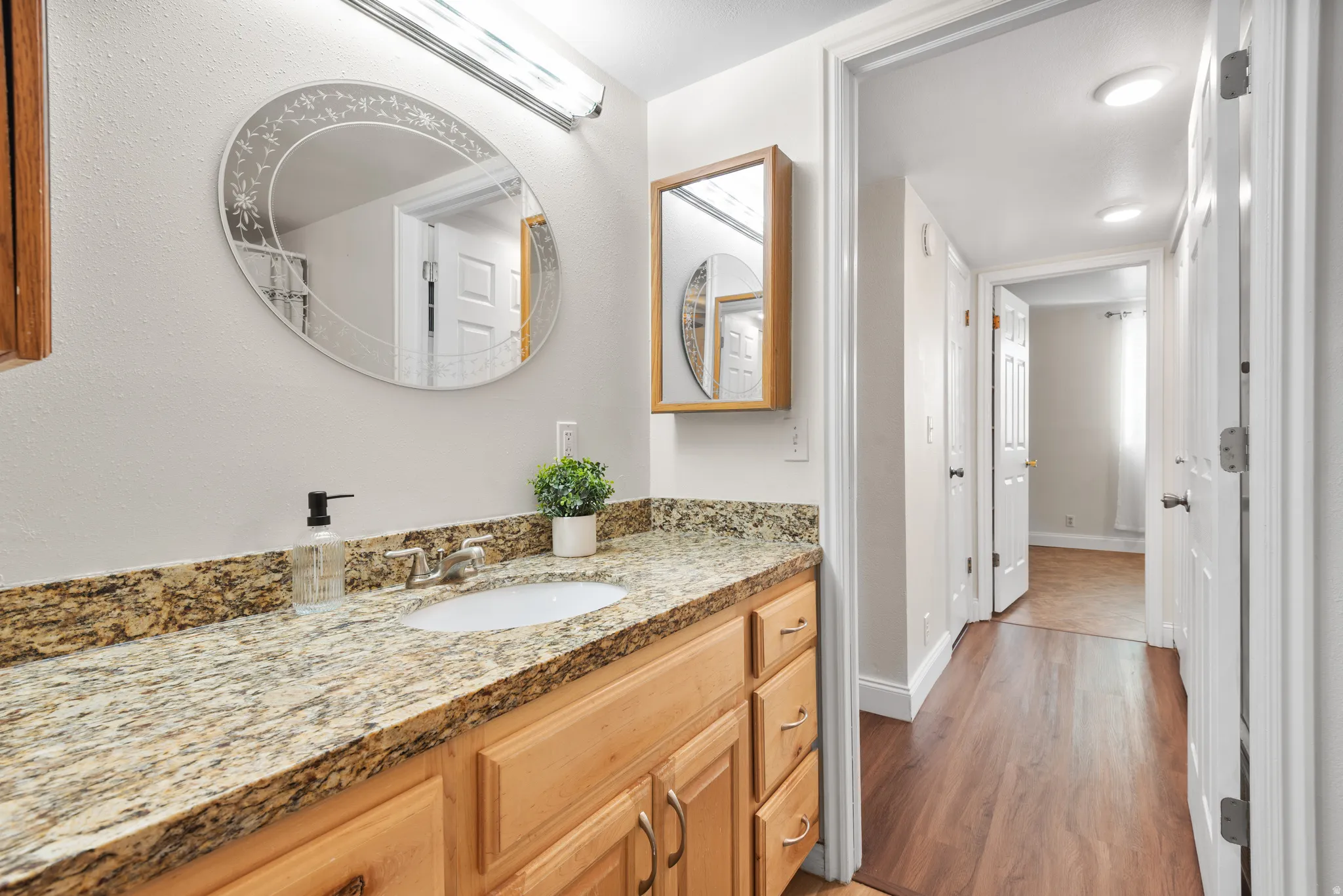 Bathroom vanity with light wood cabinetry, a granite-finish countertop, and an undermount sink