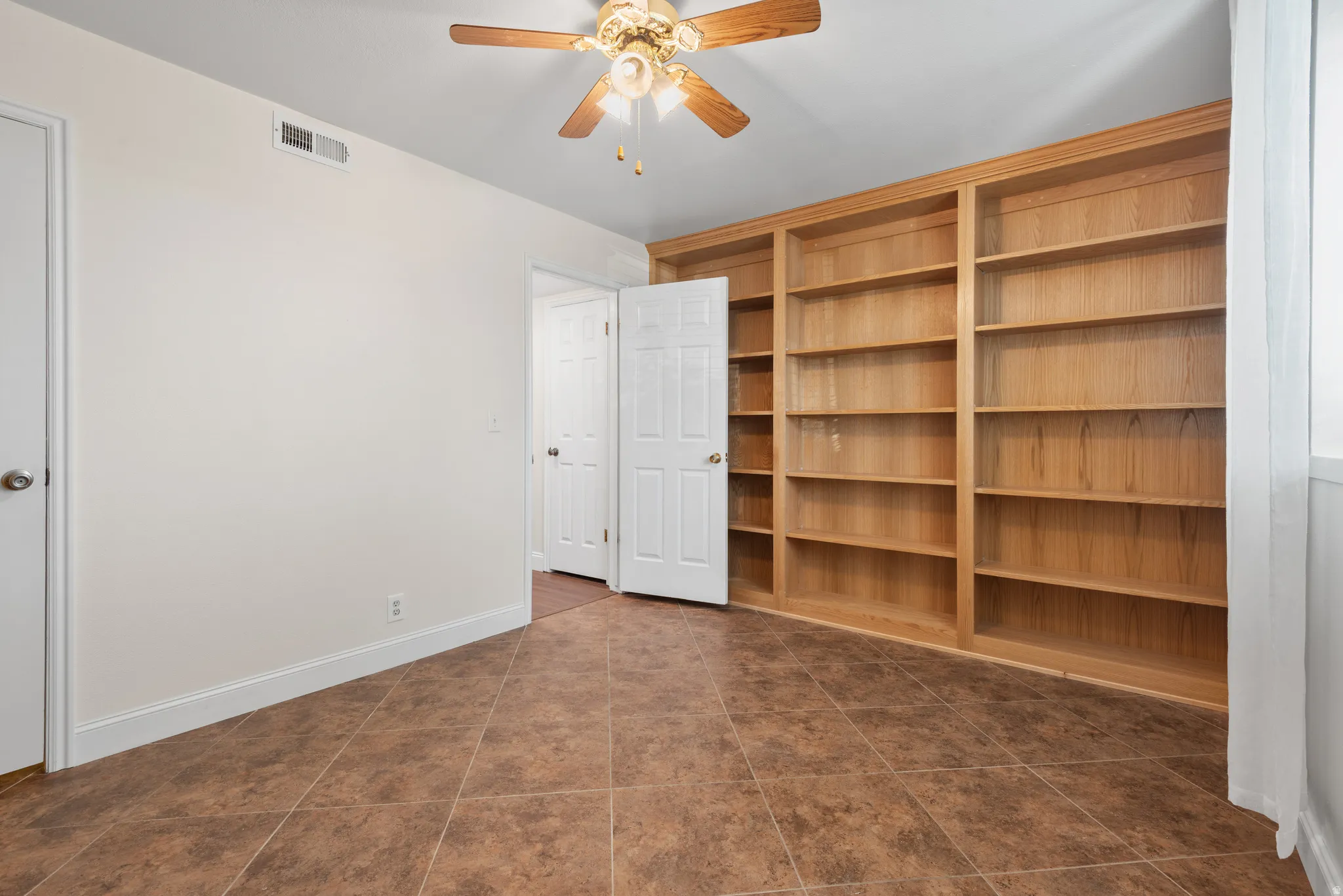 Room featuring extensive built-in wooden shelving, a ceiling fan with integrated lighting, and tile flooring