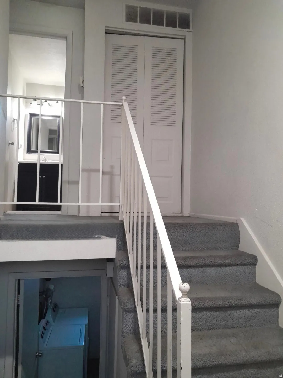 Carpeted staircase with white metal railing, featuring louvered bi-fold doors and an overhead vent