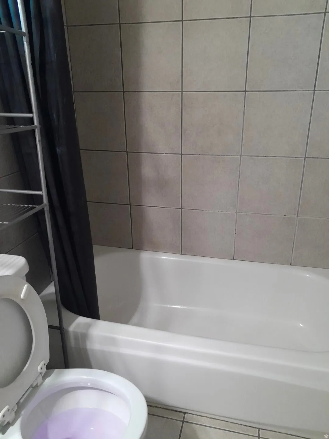 White bathtub with neutral-toned tiled surround and coordinating floor tiles