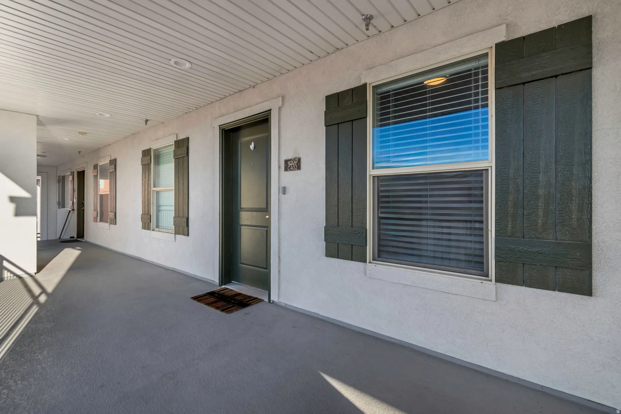 Exterior entry featuring a dark-paneled door, textured white siding, and decorative dark shutters