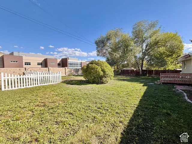 Expansive yard featuring a white picket fence, mature trees, and a wooden deck