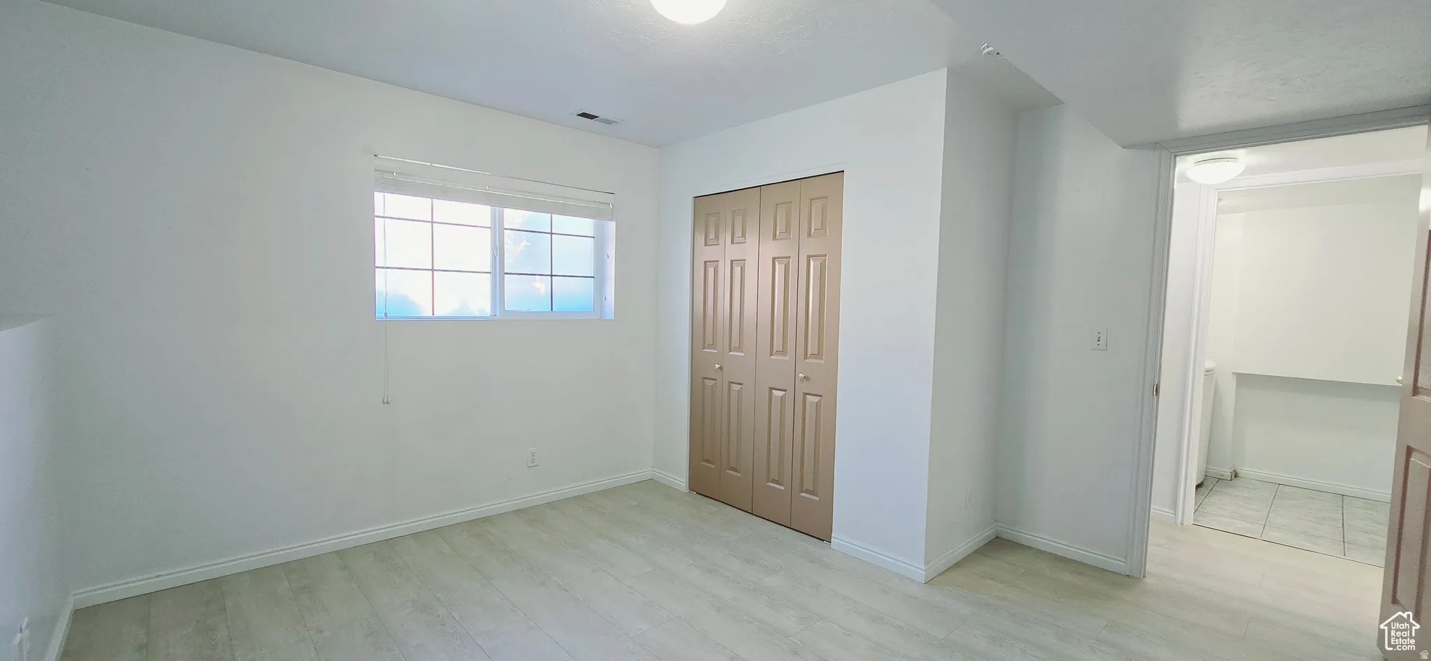 Bright room featuring wood-finish flooring, a window with horizontal blinds, and a bi-fold closet door
